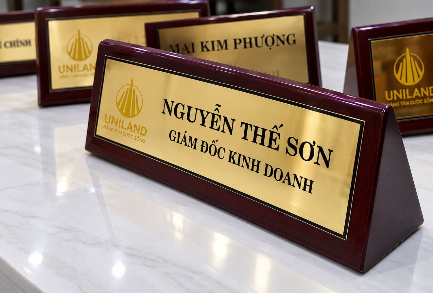 Biển chức danh để bàn inox mạ vàng đế gỗ mun đỏ, khắc tên Nguyễn Thế Sơn - Giám đốc kinh doanh, thương hiệu Uniland