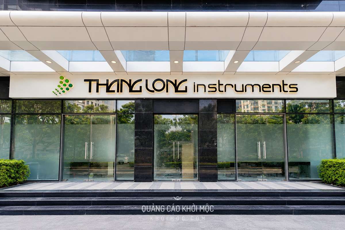 Toàn cảnh bảng hiệu Thăng Long Instruments đã hoàn thiện — nền alu trắng nổi, chữ đen bóng, logo xanh lá