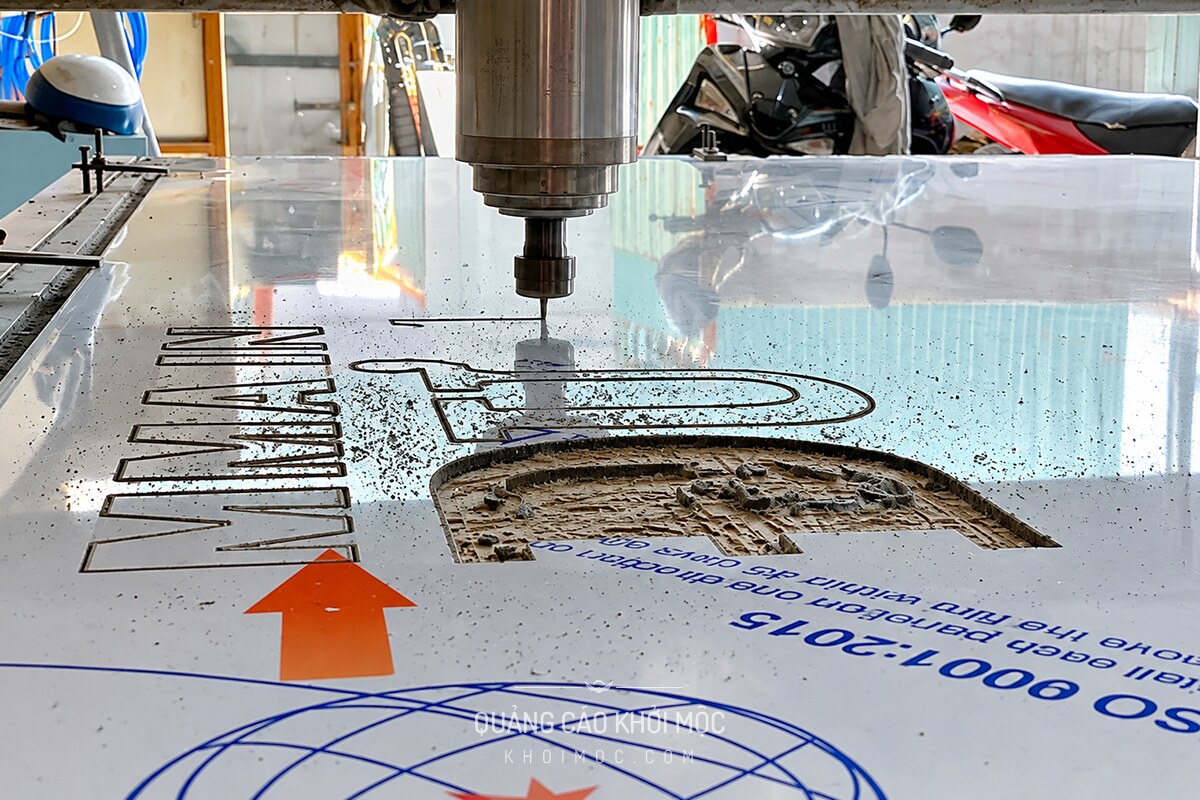 Cận cảnh mũi CNC đang cắt ký tự chữ nổi alu trên tấm nhôm