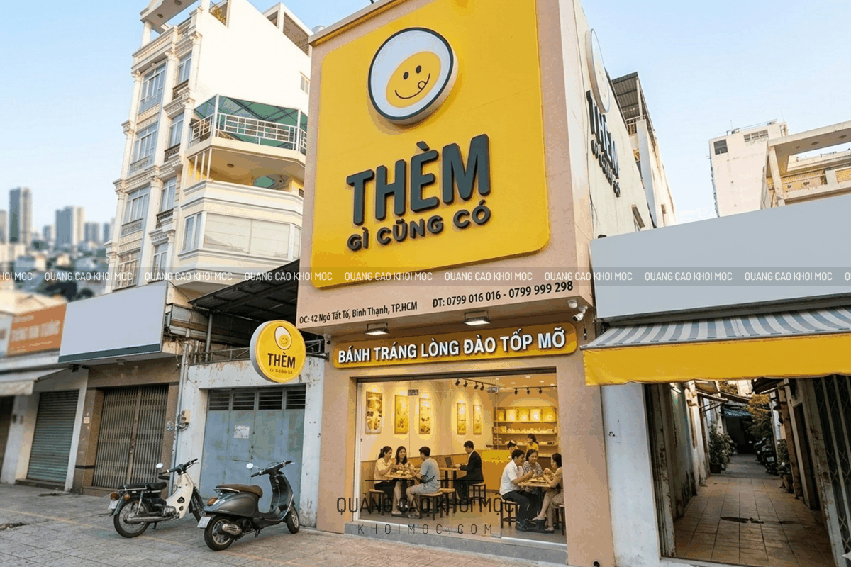 bảng hiệu alu Thèm Coffee nền vàng kết hợp icon mặt cười tạo điểm nhấn nhận diện ban ngày